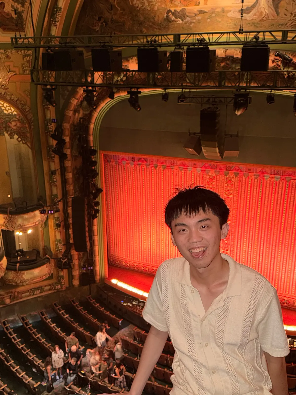 Alen Hsiao in a Broadway theatre balcony, the red curtain behind.