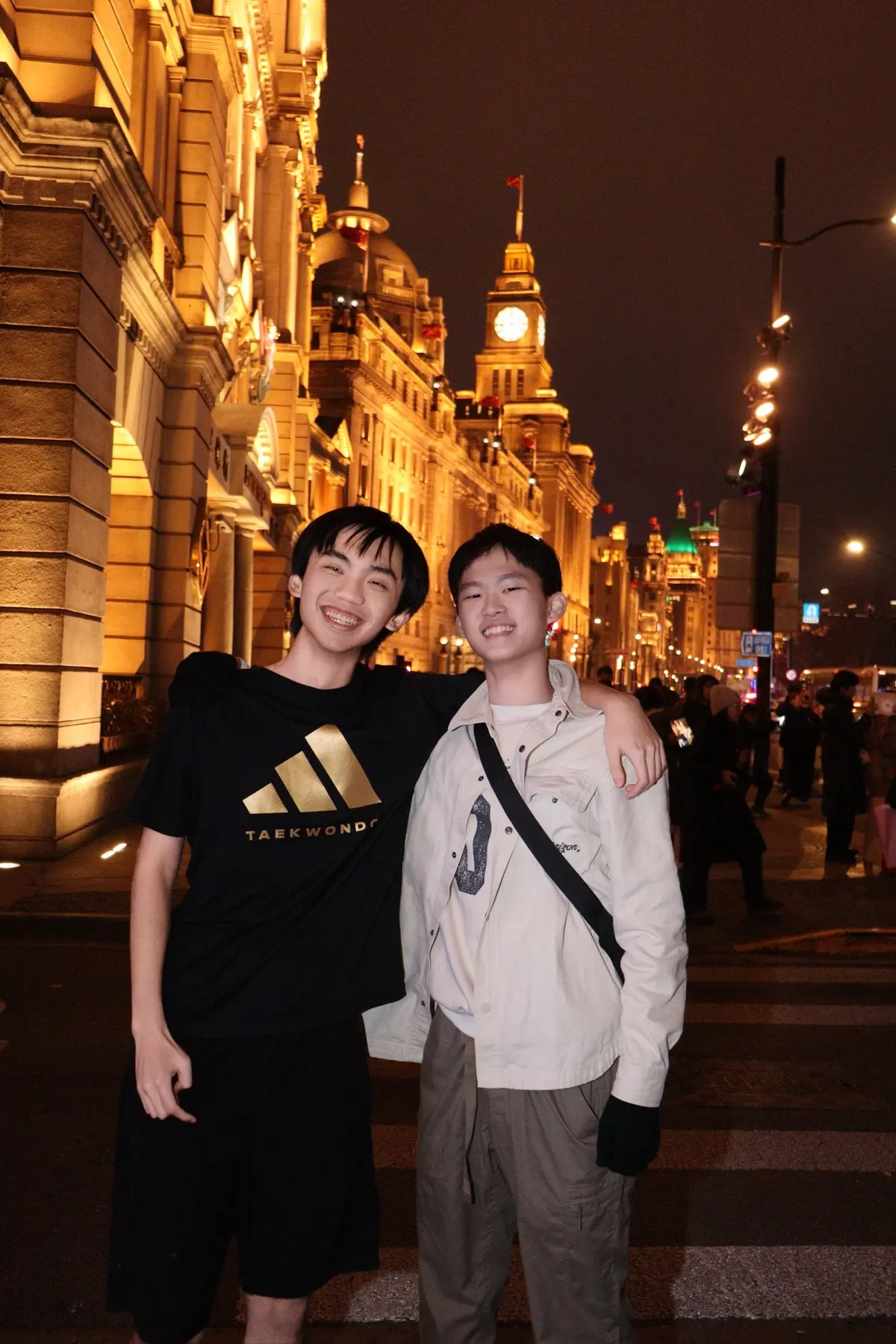 Alen Hsiao with another person at night in Shanghai, lit buildings behind them.